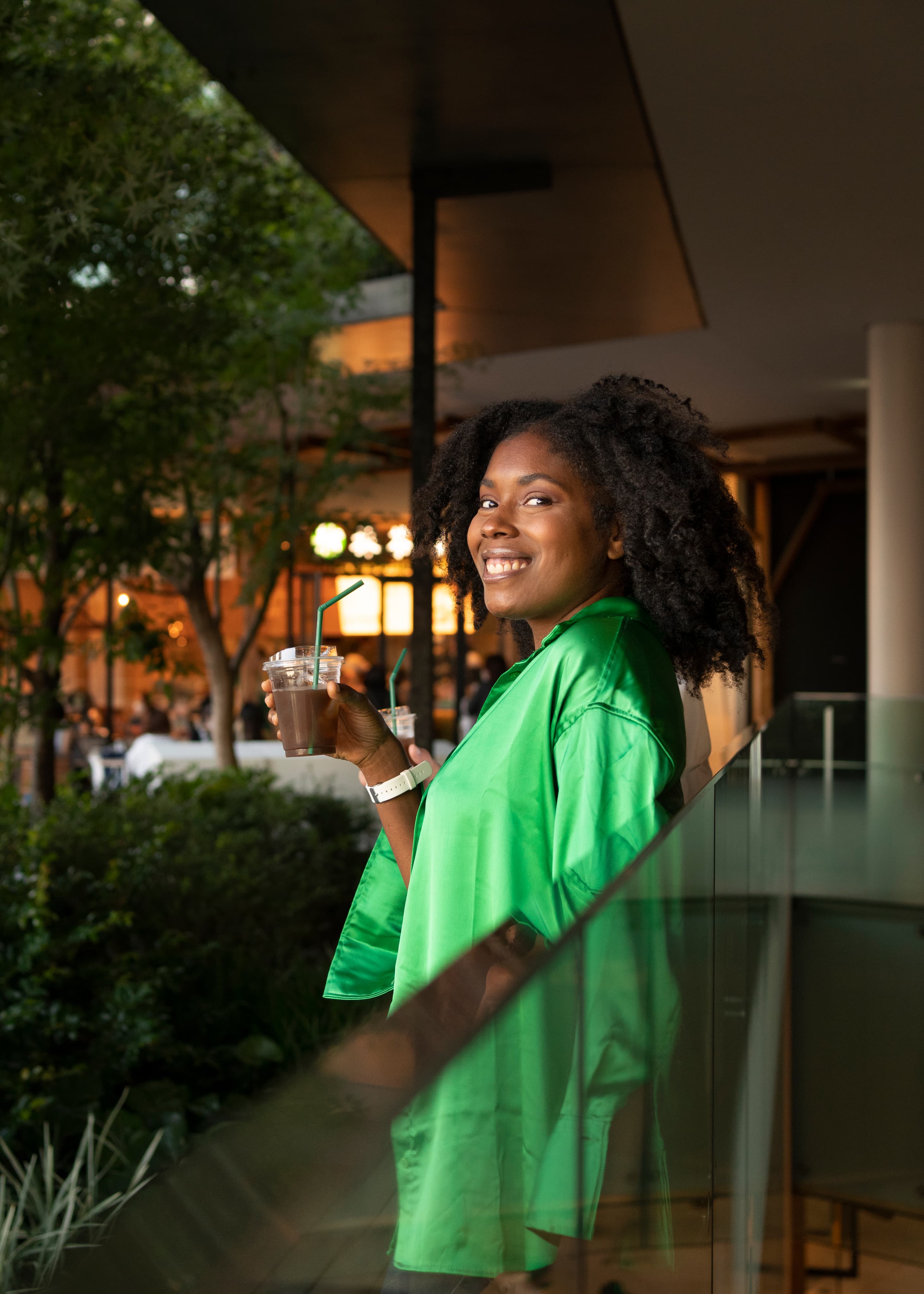 Woman standing with a drink in a green outfit.