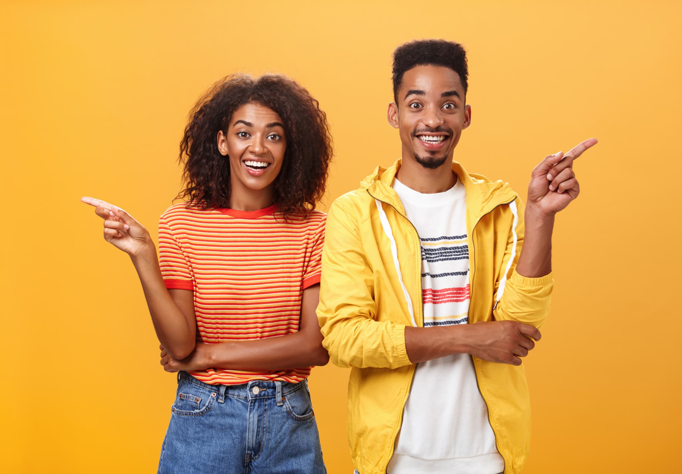 Two smiling people pointing, on a yellow background